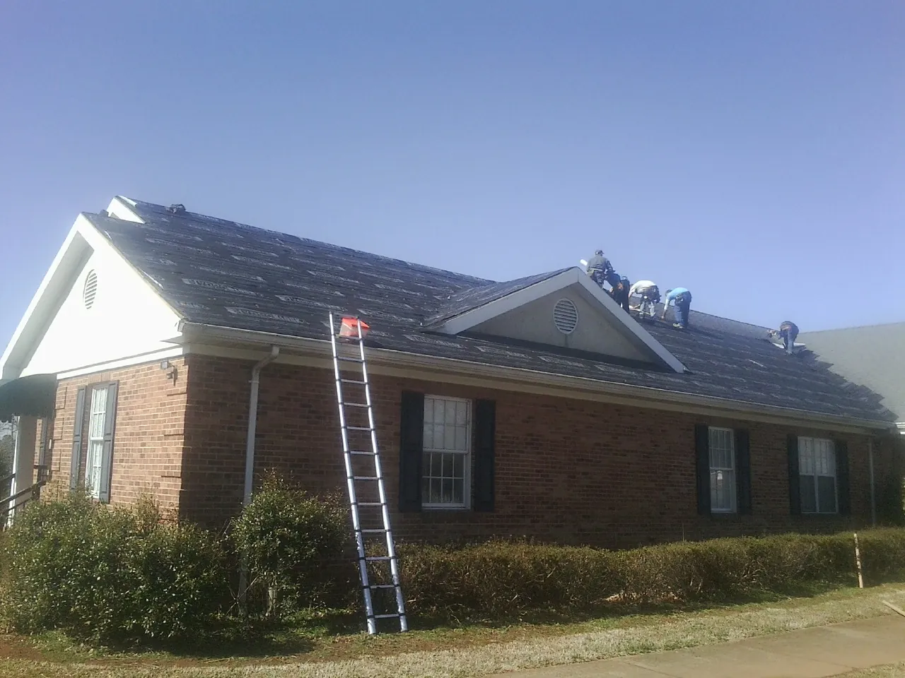 Crew tearing shingles off a brick ranch roof with a ladder set — Emergency Roof Repair work by our crew in Mutual