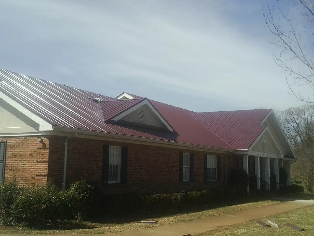 Red metal roof with gabled entries on a long brick building, from a Hail Damage Roof Repair job in Mutual