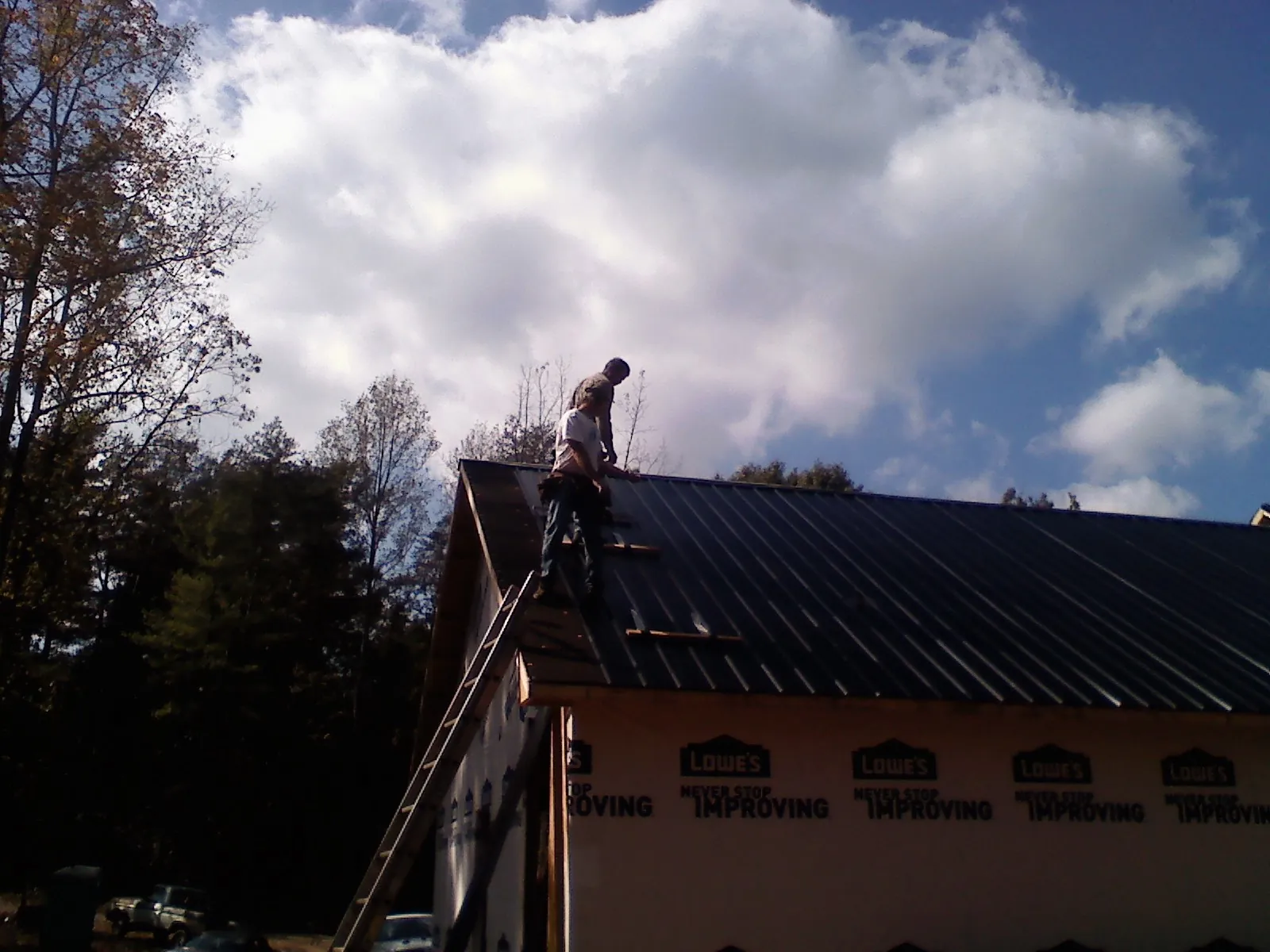Roofer fastening dark metal panels high against a cloudy sky, from a Roof Inspection job in Mutual