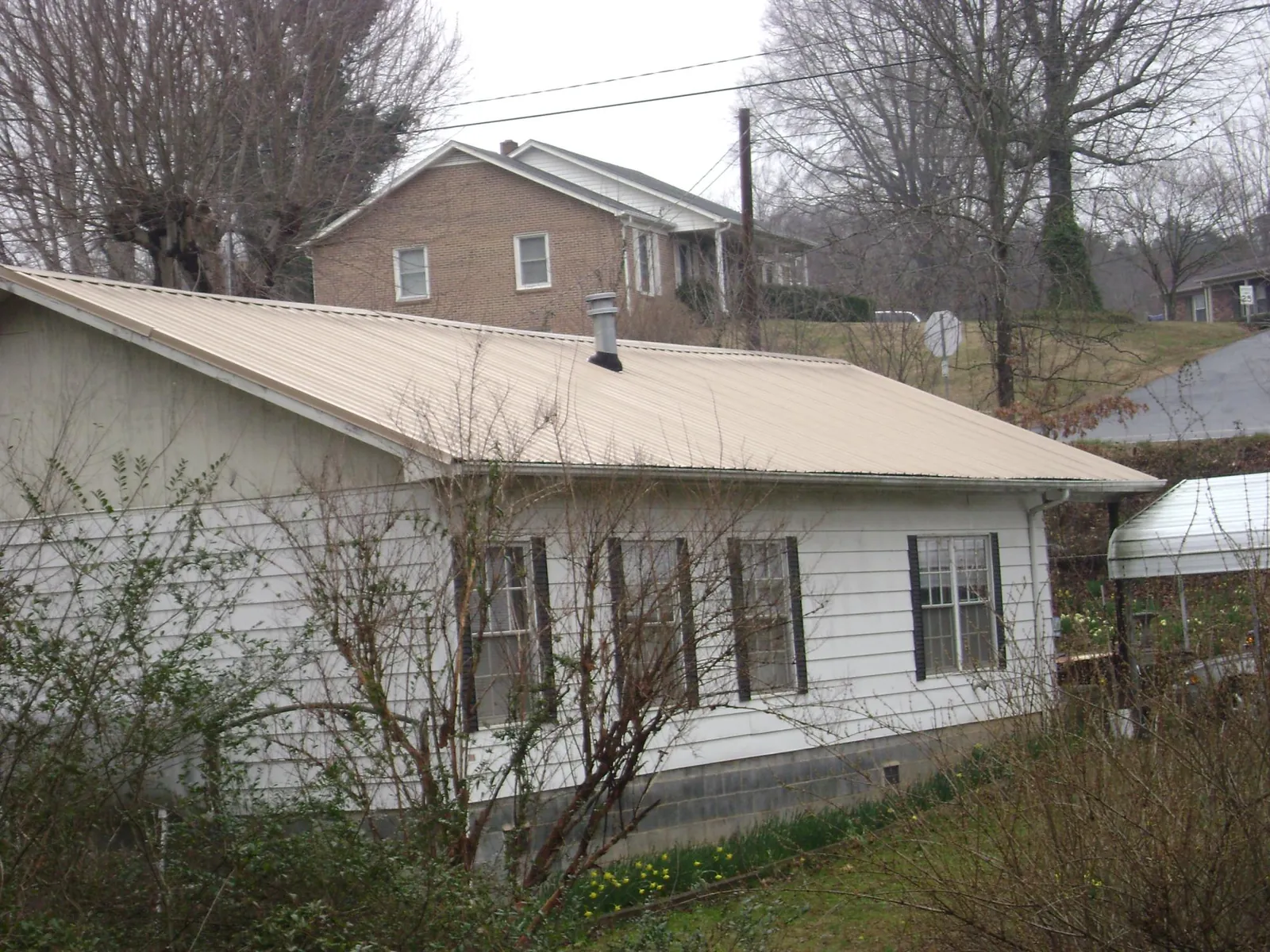 Tan metal roof on a white sided house set into a hillside — Commercial Roofing by Roofing Brothers in Mutual